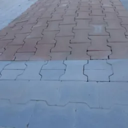 Ułożona, dwukolorowa kostka brukowa typu 'I': szara i czerwona, z widoczną przecinarką do kostki brukowej w lewym górnym rogu.