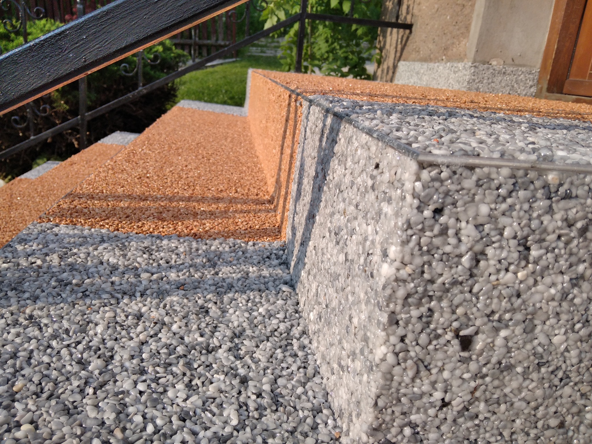 Schody zewnętrzne wykończone dwoma kolorami drobnych kamyczków zatopionych w żywicy, z metalowym obramowaniem krawędzi.