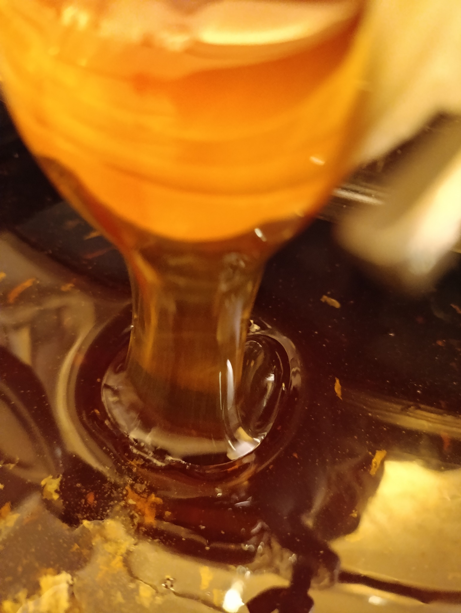 Gęsty, bursztynowy płyn spływa, tworząc wirujące refleksy w naczyniu. Zbliżenie na proces nalewania, ukazujące lepką konsystencję i bogaty kolor.