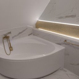 MiAA Budownictwo Mariusz Abramek - Narożna wanna z hydromasażem w łazience z marmurowymi płytkami i złotą armaturą, podświetlona mozaiką LED