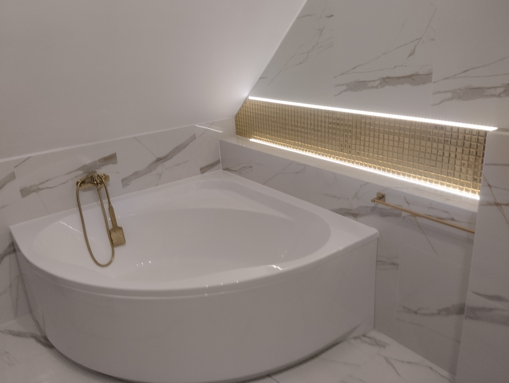 Narożna wanna z hydromasażem w łazience z marmurowymi płytkami i złotą armaturą, podświetlona mozaiką LED