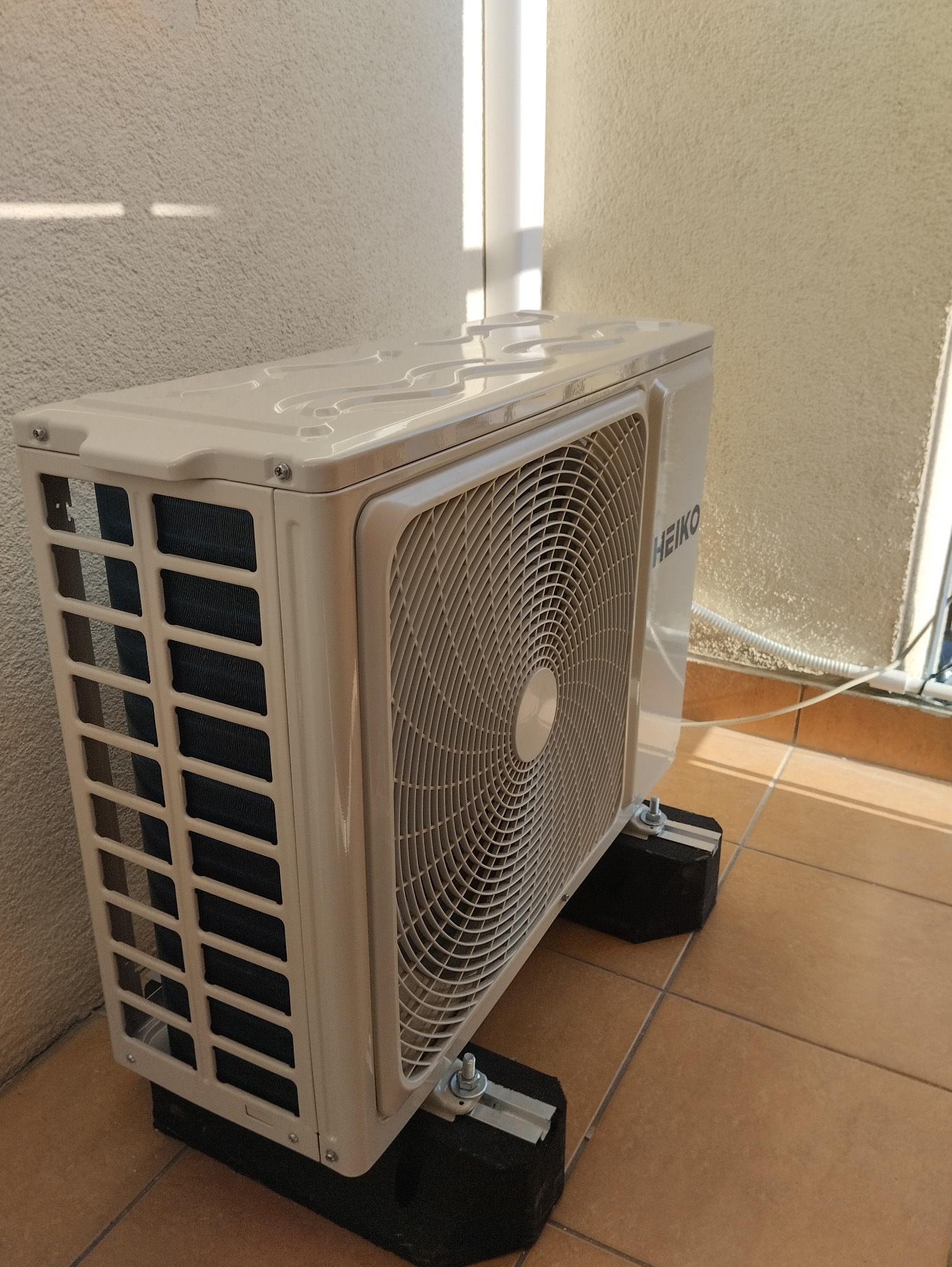 Zamontowana jednostka zewnętrzna klimatyzacji HEIKO na balkonie, przymocowana do podłoża za pomocą specjalnych wsporników antywibracyjnych.