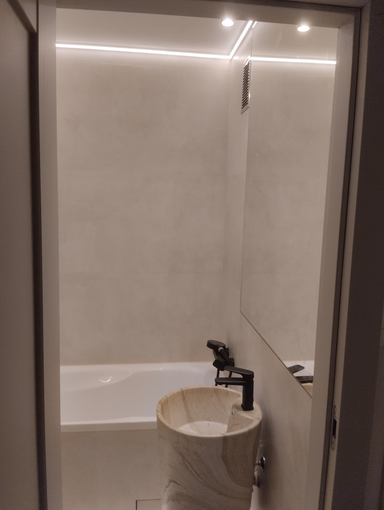 Nowoczesna łazienka z wolnostojącą umywalką z kamienia i czarną armaturą. W tle widoczna wanna i subtelne oświetlenie LED. Minimalistyczny design.