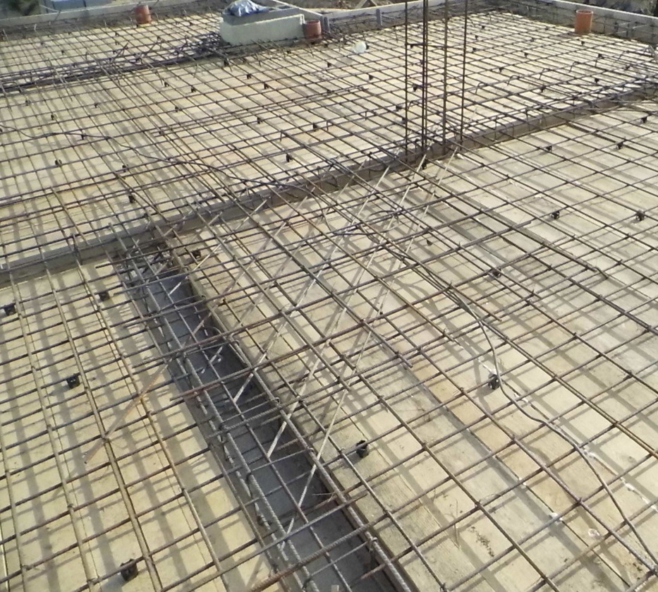 Zbrojenie stropu budynku w trakcie budowy, widoczne siatki z prętów stalowych i elementy dystansowe. Przygotowanie do wylewania betonu.