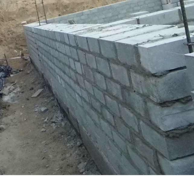 Wznoszenie fundamentów z bloczków betonowych na placu budowy. Widoczne zbrojenie i świeże spoiny. Ujęcie z dołu, podkreślające solidność konstrukcji.