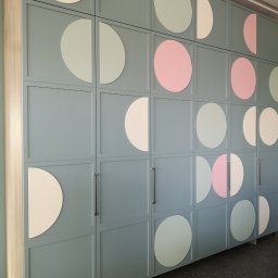 Krzysztof Pęczek, F.H.U. AGMA - Niebieska szafa z geometrycznym wzorem z kolorowych kół, widoczna z perspektywy. Minimalistyczny design, metalowe uchwyty, jasne tło.