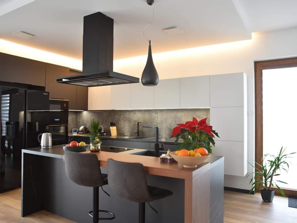 Nowoczesna kuchnia z wyspą i czarnym okapem. Białe szafki górne, szare ściany. Na wyspie owoce i dekoracje świąteczne. Minimalistyczny design z oświetleniem LED.