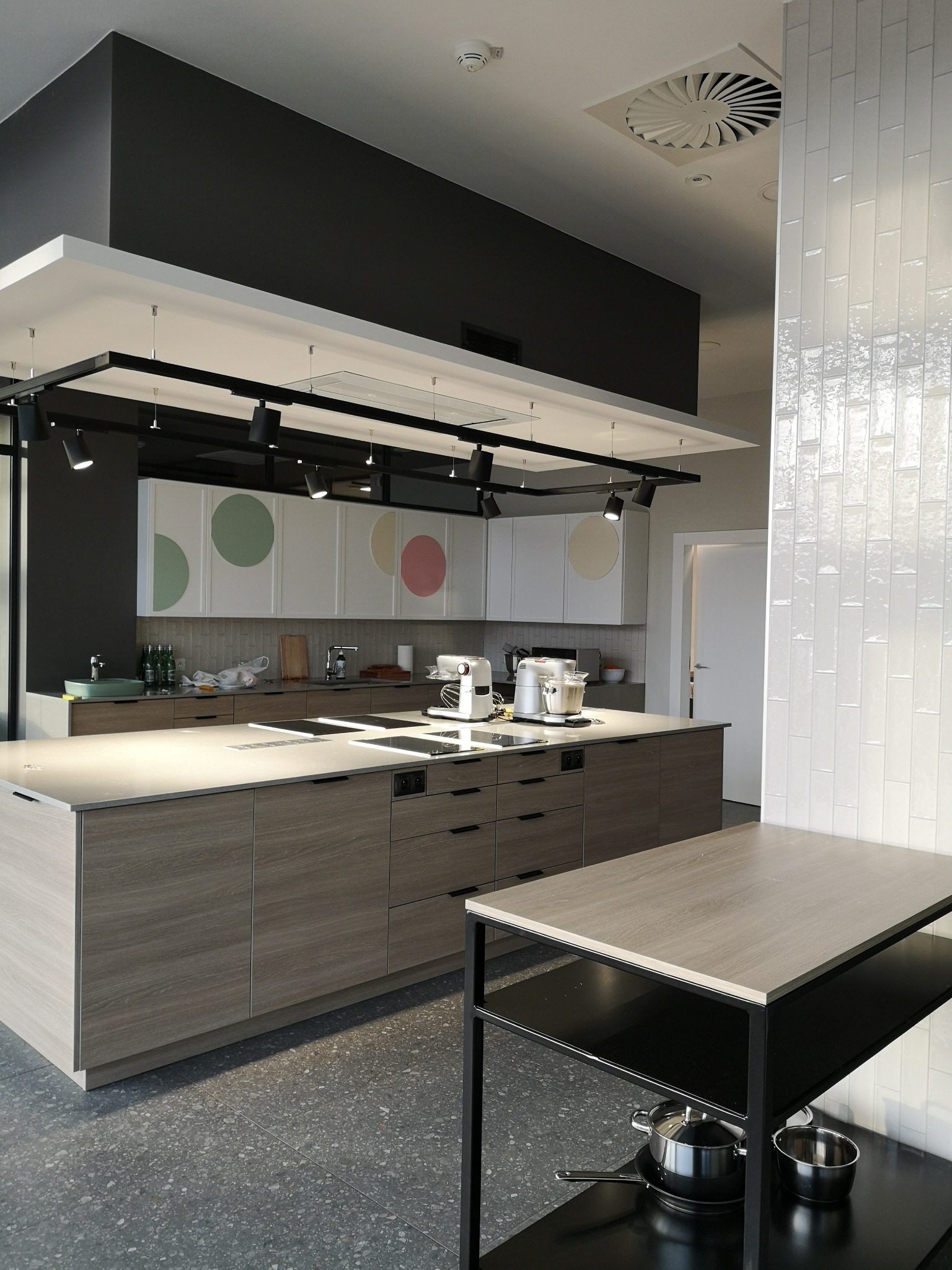Nowoczesna kuchnia z wyspą i szafkami z okrągłymi dekorami. Nad wyspą oświetlenie punktowe. Na blacie mikser i inne akcesoria kuchenne. Na podłodze lastryko.