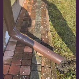 Malowanie dachów , mycie kostki oraz elewacji - Brudna kostka brukowa przy budynku z widocznym odpływem rynnowym, stan 'przed' czyszczeniem.