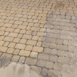 G&G SHOP MARZENA GRYGORUK - Częściowo umyta, beżowa kostka brukowa przed brązową, drewnianą bramą garażową; widoczna różnica w kolorze między czystą a brudną powierzchnią kostki.