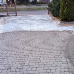 Częściowo umyta kostka brukowa przed bramą wjazdową, widoczna różnica w kolorze czystej i brudnej powierzchni.