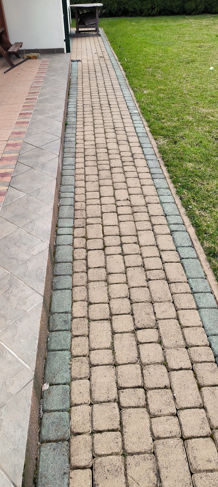 Długa ścieżka z kostki brukowej w odcieniach beżu i szarości, oddzielająca trawnik od tarasu z płytkami, widok z góry.