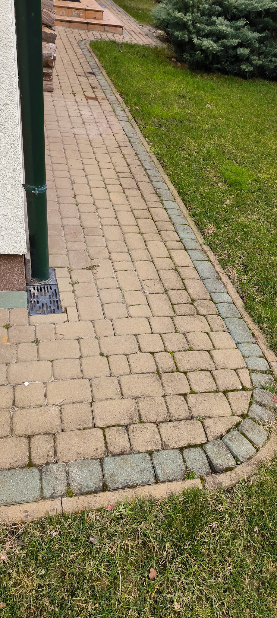 Żółta kostka brukowa przed domem w Białymstoku, widoczna zieleń trawy i rynna spustowa.