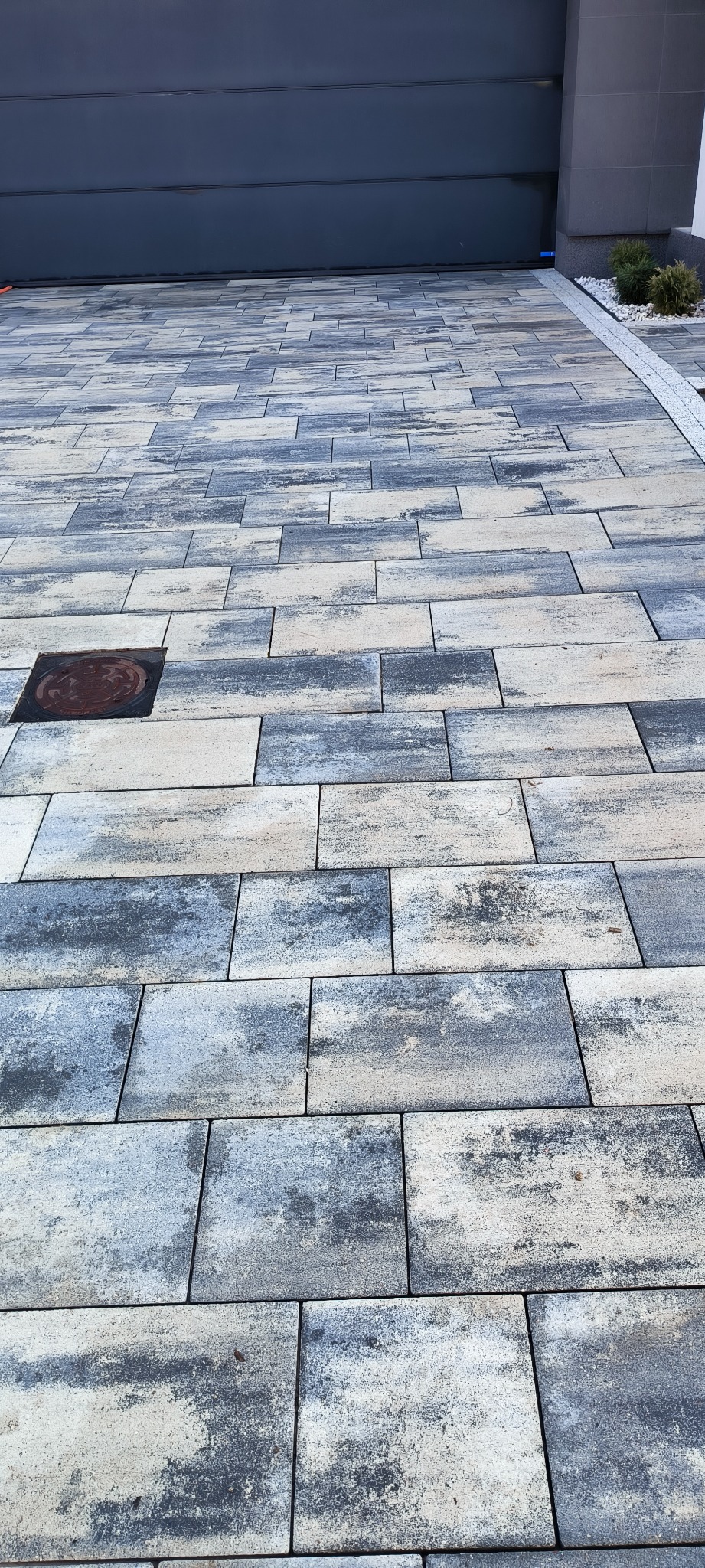 Ułożona szara kostka brukowa przed garażem z widoczną studzienką kanalizacyjną i odpływem liniowym.