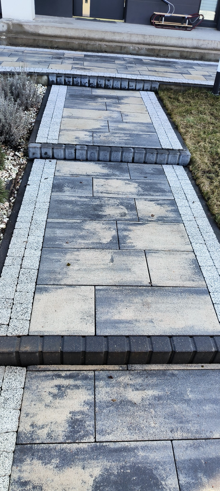 Schody i ścieżka z kostki brukowej w odcieniach szarości, obrzeża wyłożone drobnym, jasnym kamieniem, widok z góry.