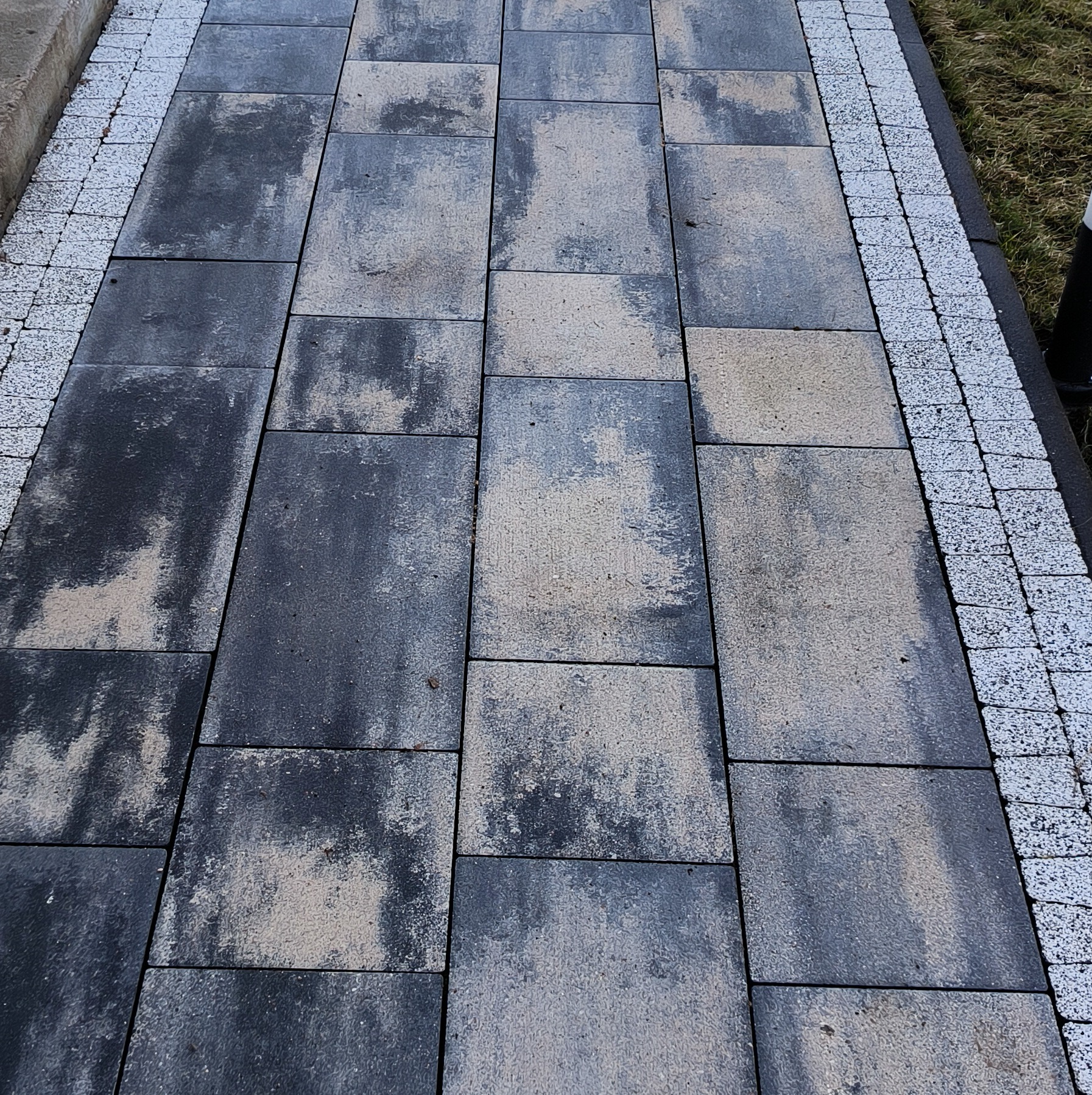 Ułożona kostka brukowa w odcieniach szarości z jasną obwódką z drobnej kostki, widoczne ślady po czyszczeniu.