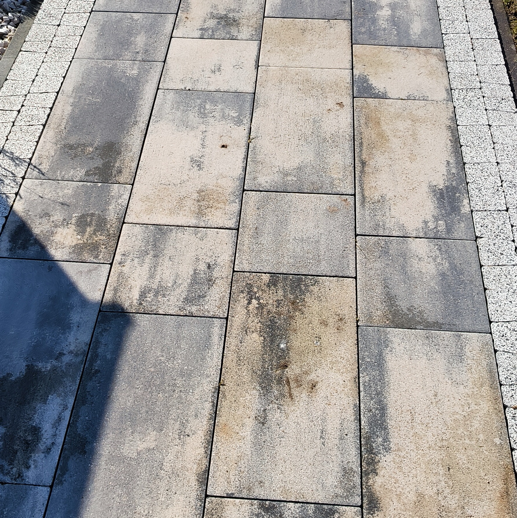 Szara kostka brukowa z widocznymi śladami zabrudzeń i cieniem, obrzeża z drobnej, jasnej kostki.