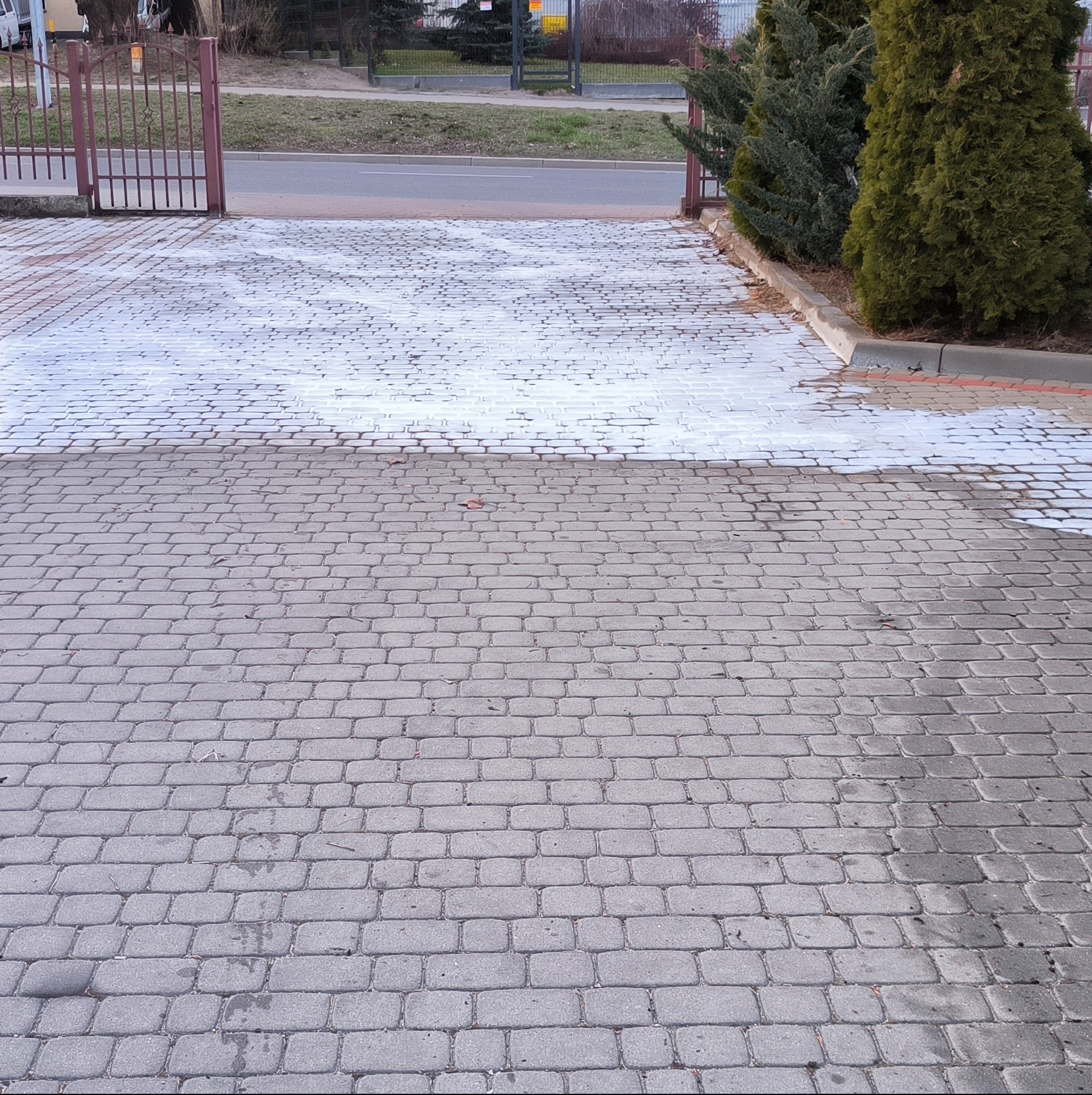 Częściowo umyta kostka brukowa w Białymstoku, widoczne różnice w kolorze przed i po czyszczeniu, brama w tle.