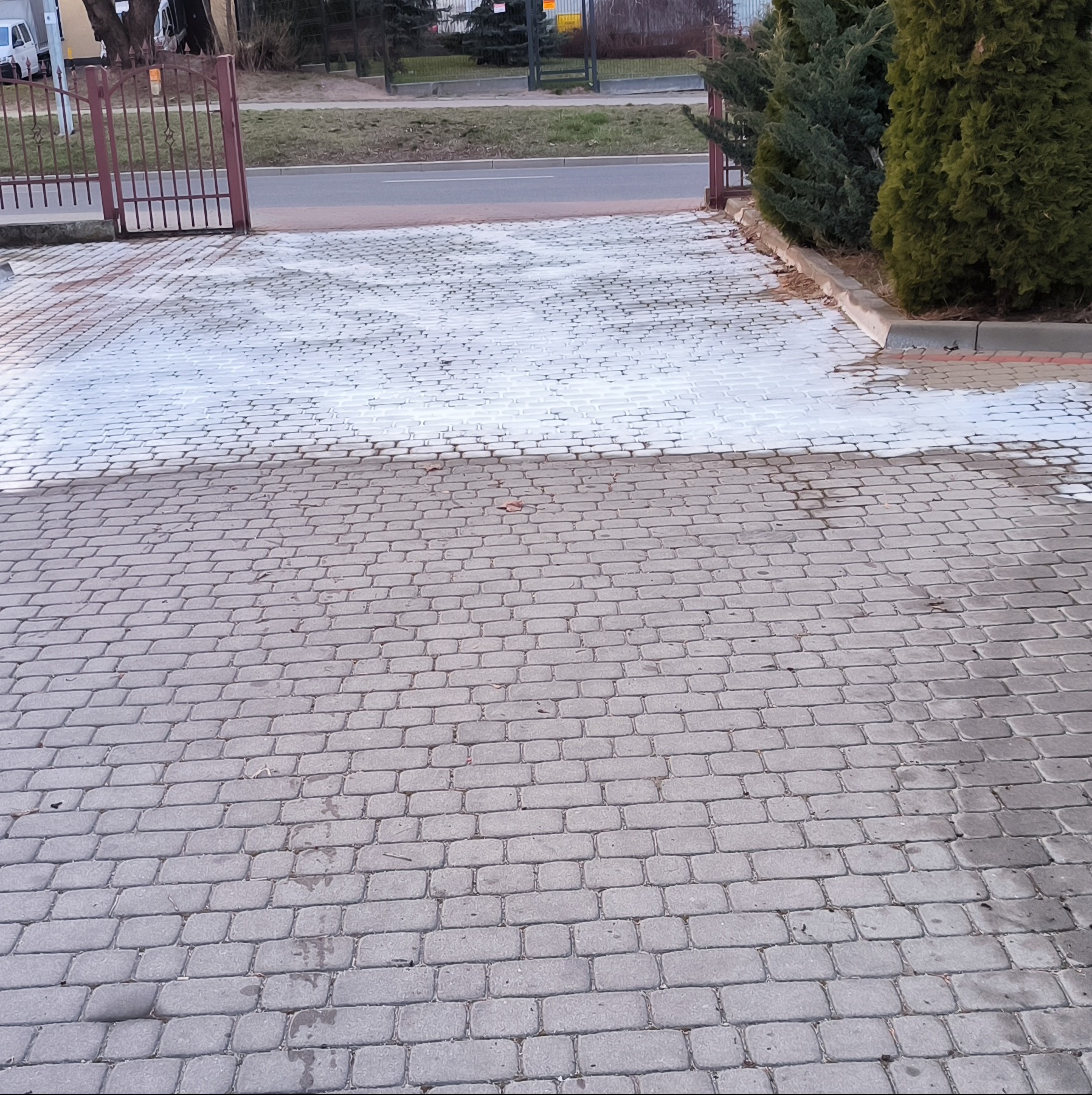Częściowo umyta kostka brukowa przed bramą wjazdową, widoczna różnica w kolorze czystej i brudnej powierzchni.