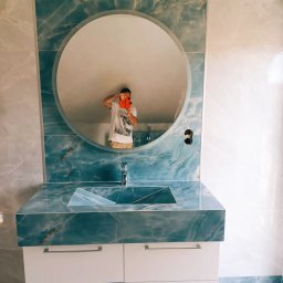 Rafi-Bud - Nowoczesna łazienka z umywalką nablatową z niebieskiego marmuru, okrągłe lustro z odbiciem fotografa, białe szafki pod umywalką i marmurowe płytki na ścianach.