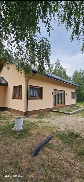 Dom jednorodzinny z beżową elewacją, brązowymi oknami i czarną rynną, widok z zewnątrz w letni dzień.