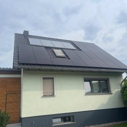 SolarPro Davyd Lytvynets - Dom z panelami słonecznymi na dachu, widok z dołu. Część paneli jest w kolorze czarnym, a część w kolorze szarym. Widoczne okno dachowe i fragment ogrodu.