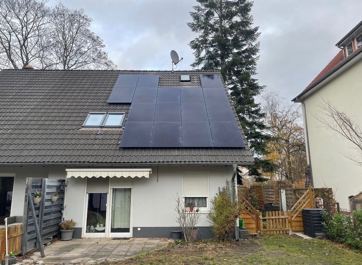 Panele słoneczne na dachu domu jednorodzinnego z szarą dachówką i oknami dachowymi, antena satelitarna, widok z poziomu ogrodu w pochmurny dzień.