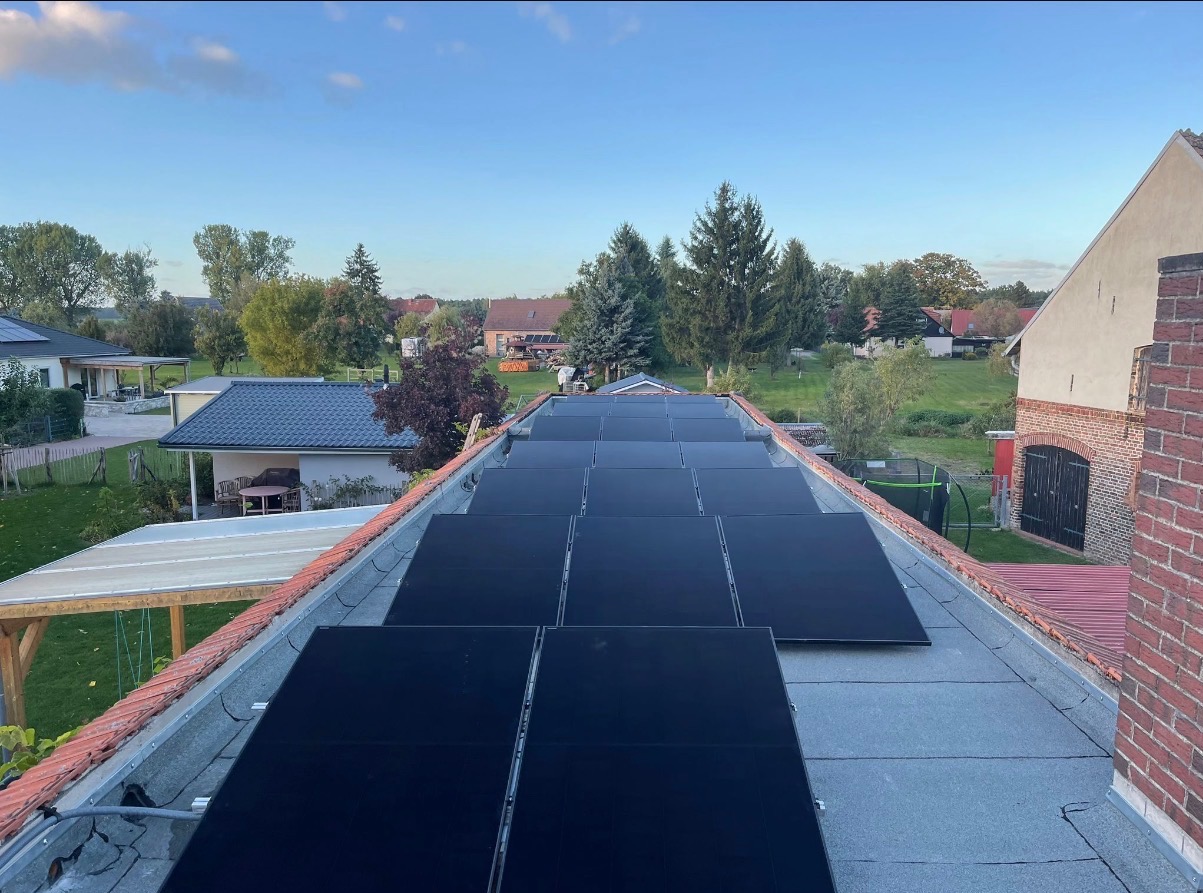 Panele słoneczne na dachu domu jednorodzinnego, widok z góry na tle zieleni i zabudowań. Instalacja fotowoltaiczna w otoczeniu wiejskim.