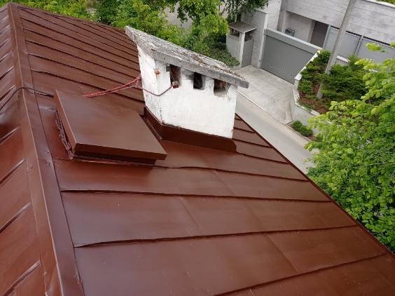 Ciemnobrązowy, metalowy dach po malowaniu, z widocznym kominem i elementami wentylacyjnymi. Ujęcie z góry, ukazujące fakturę blachy i świeży kolor.