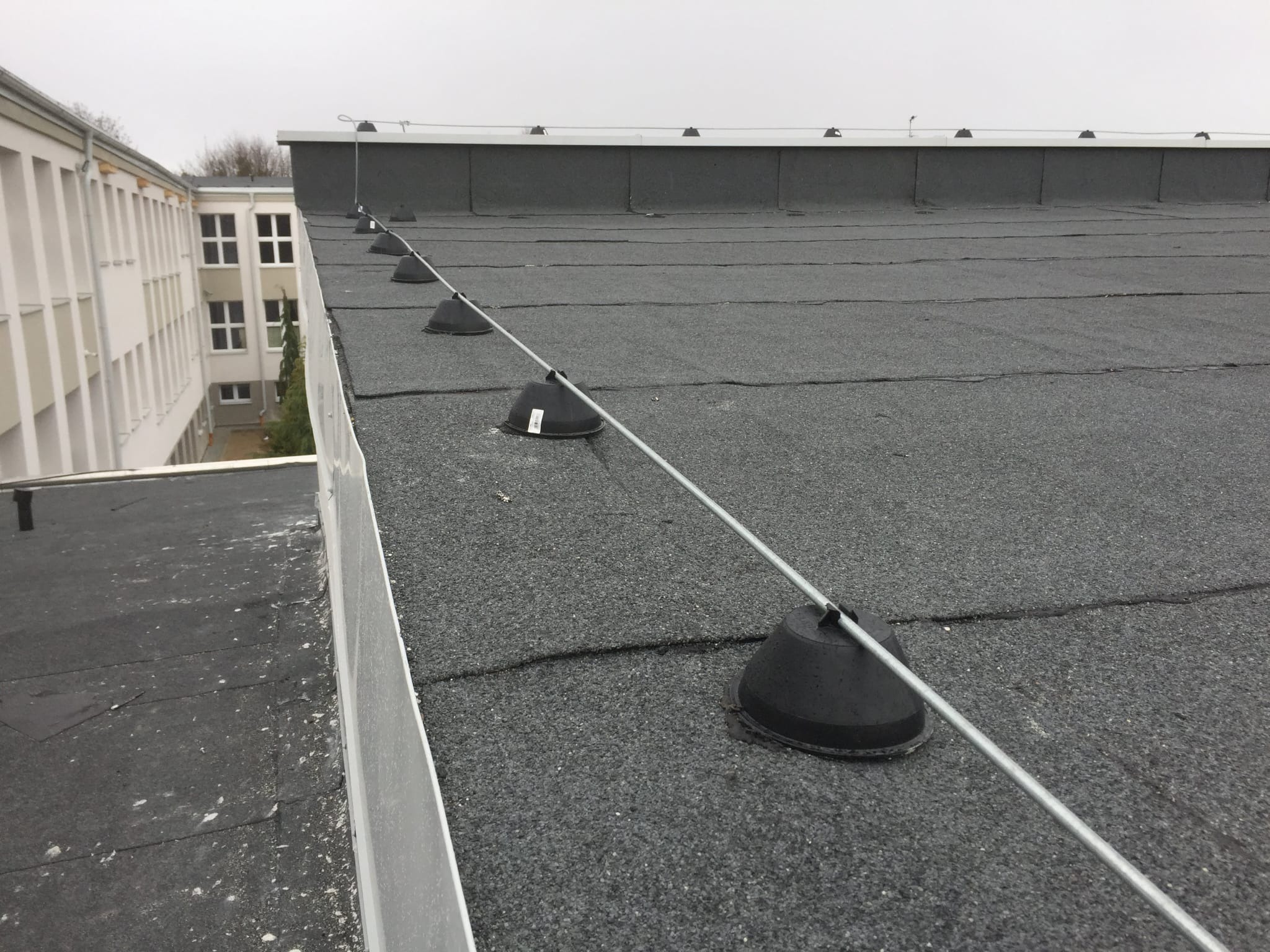 Płaski dach pokryty papą z zainstalowaną instalacją odgromową, widok z góry na szarym tle nieba.