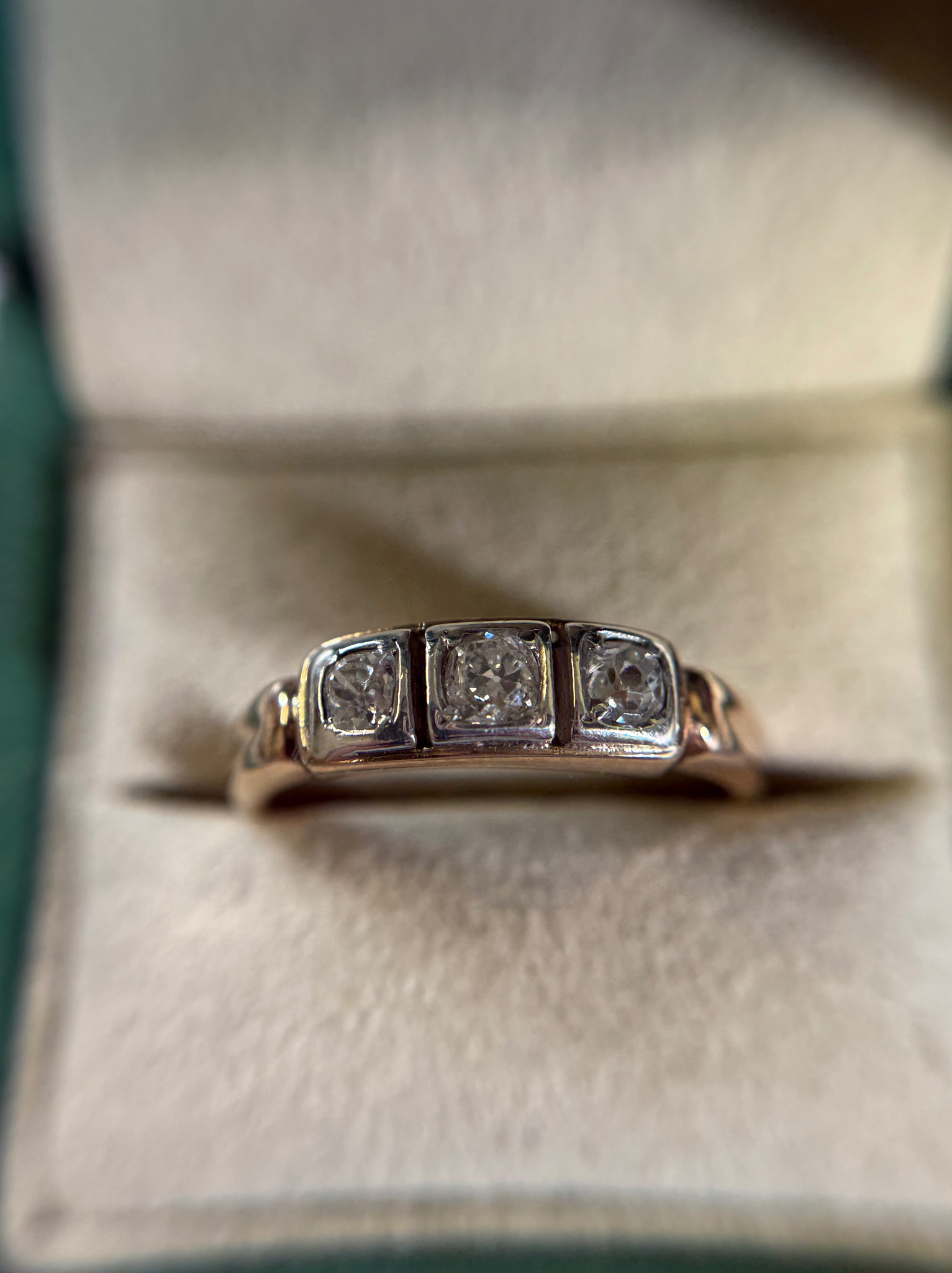 Złoty pierścionek z trzema brylantami w pudełku z kremowym wnętrzem i zieloną krawędzią, widok z bliska.