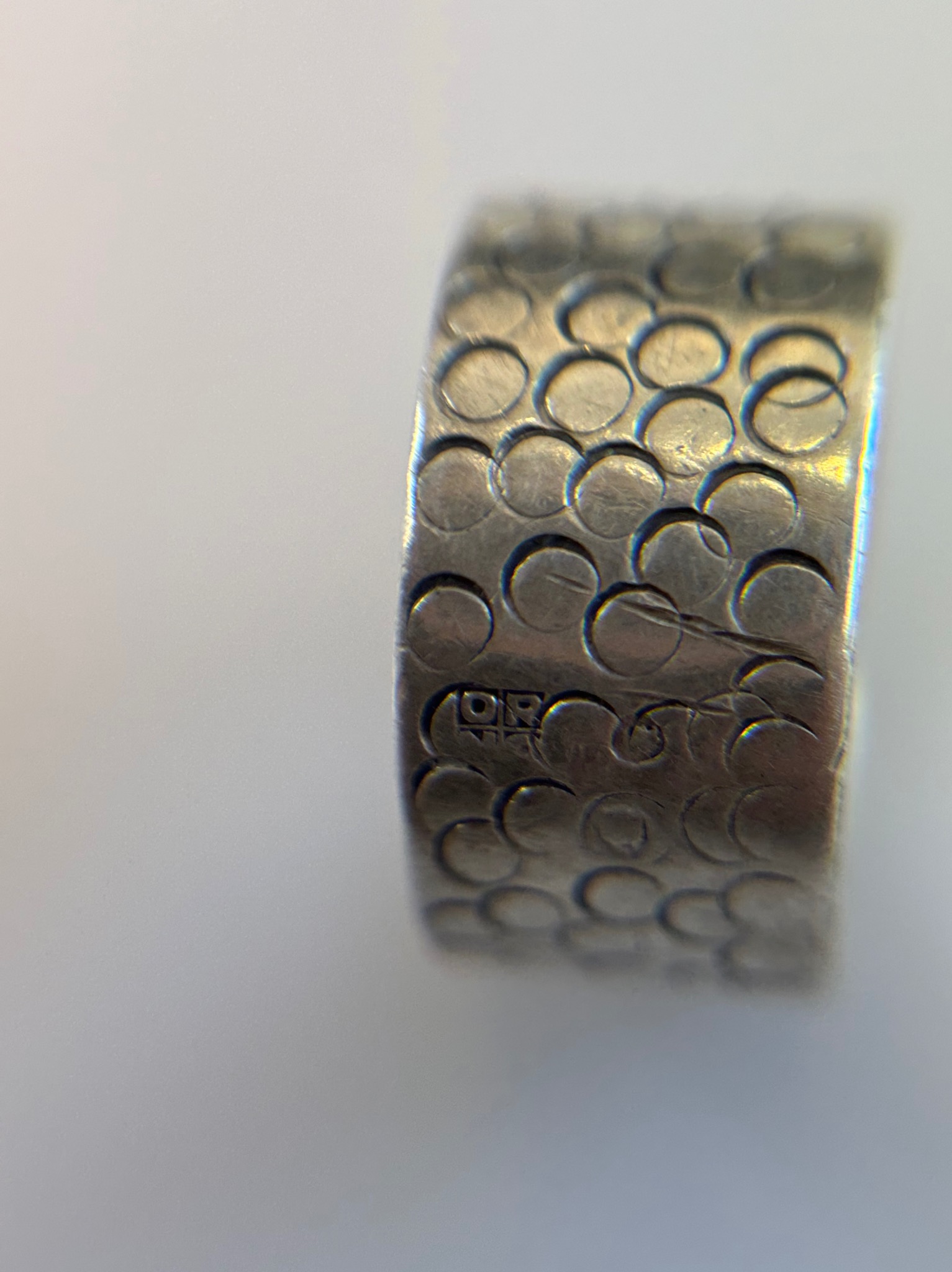 Srebrny pierścionek z wytłoczonym wzorem kół i półksiężyców, widoczne delikatne zarysowania i sygnatura.