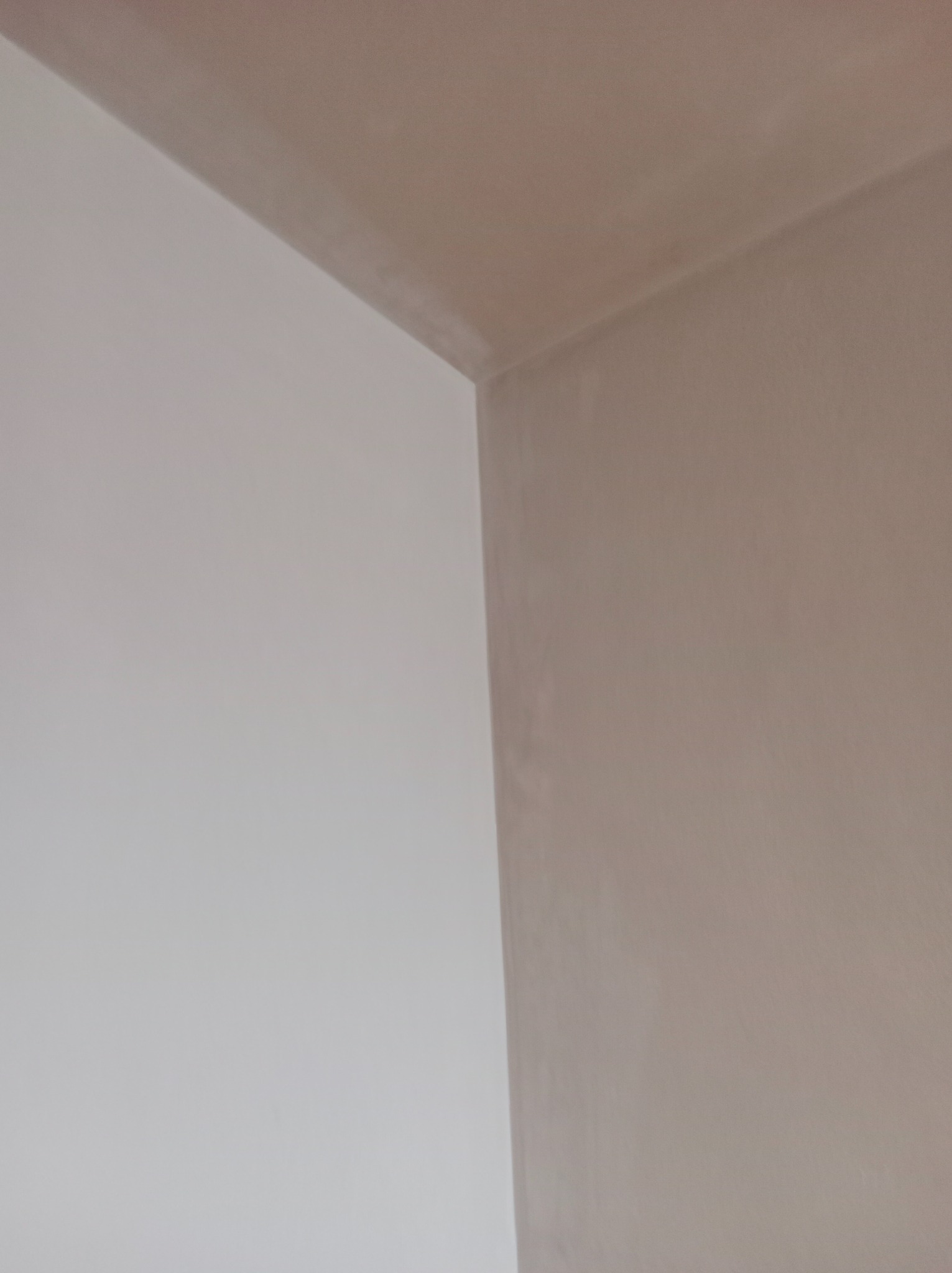 Wnętrze narożnika pokoju po nałożeniu jasnej, matowej farby na ścianę i sufit, z delikatną fakturą widoczną pod światło.