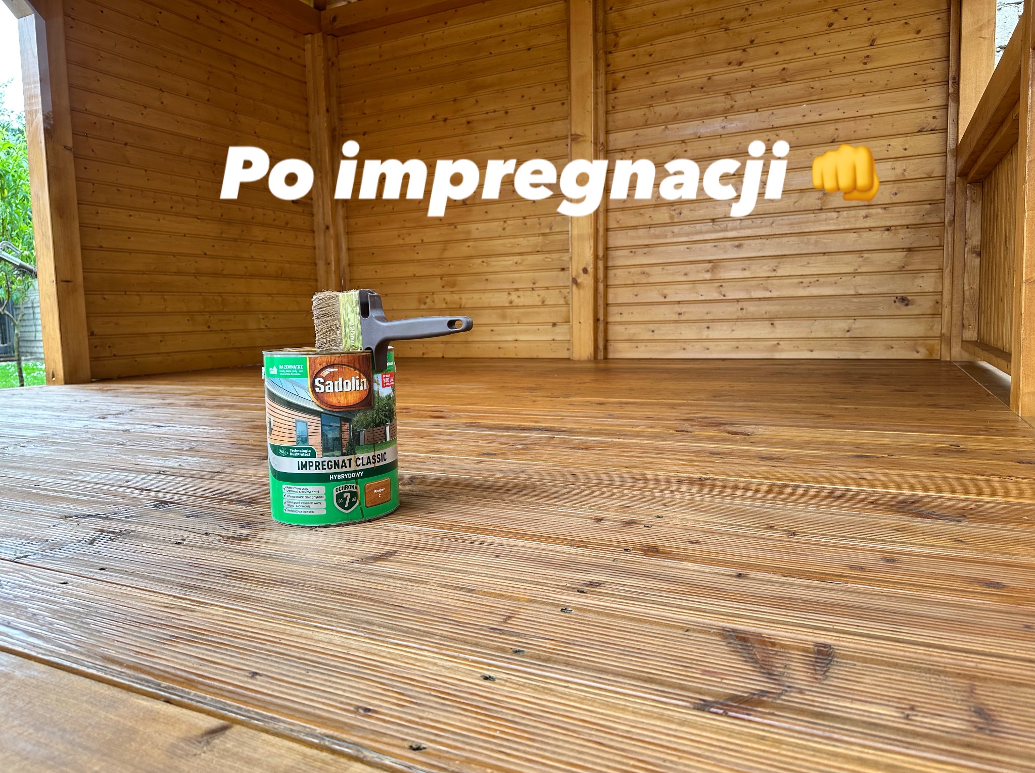 Drewniana altana po impregnacji. Widoczna puszka impregnatu Sadolin Classic i pędzel. Podłoga i ściany altany mają świeży, jednolity odcień drewna.