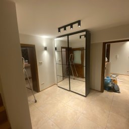 ANDRIY ANDRIISHYN - Nowoczesna szafa wnękowa z lustrami i czarnymi ramami, zamontowana w korytarzu z beżowymi płytkami. Widoczne oświetlenie sufitowe i drzwi do innych pomieszczeń.