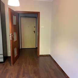 ANDRIY ANDRIISHYN - Pusty pokój po remoncie: ciemne panele podłogowe, jasne ściany i otwarte drewniane drzwi z szybkami, widok na kolejne drzwi. Lampa sufitowa w rogu.