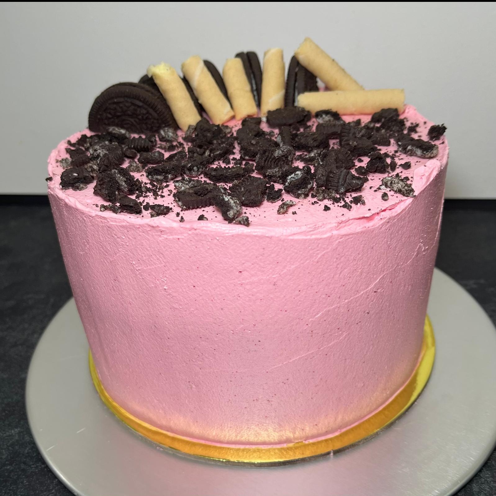 Różowy tort z kremem, posypany pokruszonymi ciastkami Oreo i ozdobiony waflami na srebrnej paterze.
