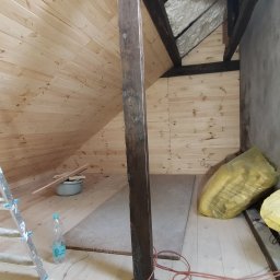 Piotr Pawlak - Adaptacja poddasza: drewniana boazeria na skośnej ścianie i suficie, widoczne krokwie, ocieplenie, kabel elektryczny na podłodze, drabina malarska i butelka wody mineralnej.