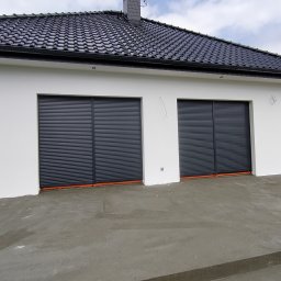 Piotr Pawlak - Biały budynek z dwoma szarymi roletami zewnętrznymi, widoczny świeżo wylany betonowy podjazd, czarny dach z dachówki ceramicznej, pochmurne niebo w tle.