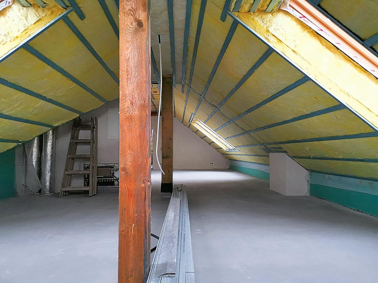 Poddasze w trakcie adaptacji: widoczne ocieplenie wełną mineralną między krokwiami, drewniane słupy konstrukcyjne, drabina oparta o ścianę, przygotowane profile metalowe na podłodze.