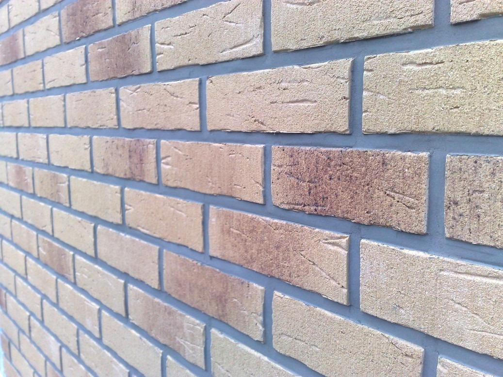 Elewacja z klinkieru w odcieniach beżu i brązu, z szarą fugą, ułożona w regularny wzór, widoczna z perspektywy.