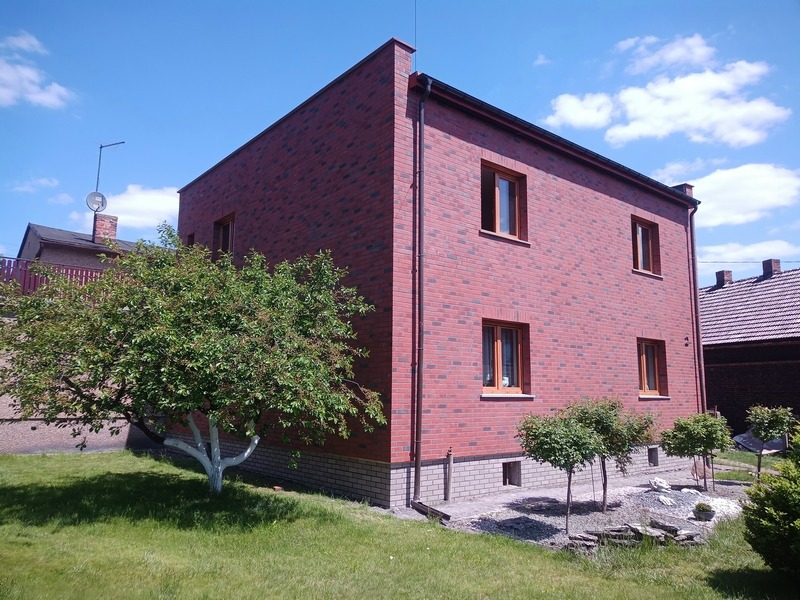 Dwukondygnacyjny dom z elewacją z czerwonej cegły klinkierowej, brązowe okna, widok z ogrodu, drzewo z pomalowanym na biało pniem.