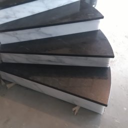 Firma Budowlano Kamieniarska Ireneusz Strzelczyk - Montaż schodów z czarnego kamienia z białymi marmurowymi podstopnicami, widoczne etapy wykończeniowe i narzędzia.