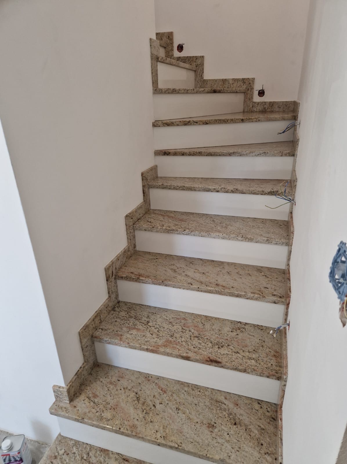 Granitowe stopnie schodowe z białymi podstopnicami, widoczne kable elektryczne wystające ze ściany, w tle białe ściany.