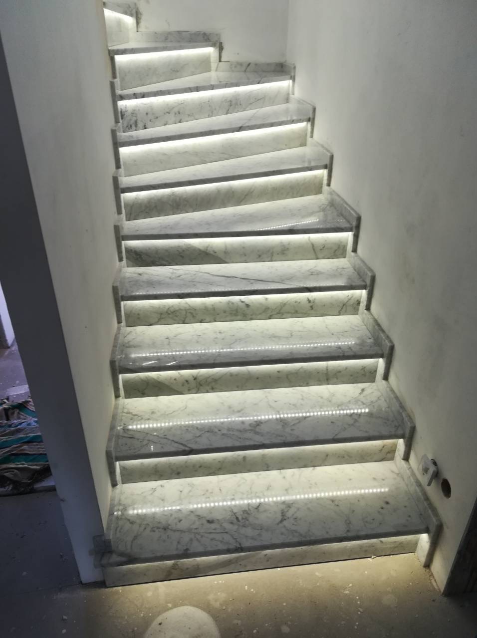 Marmurowe schody wewnętrzne z podświetleniem LED wzdłuż stopni, widok z dołu, częściowo widoczne ściany w tle.