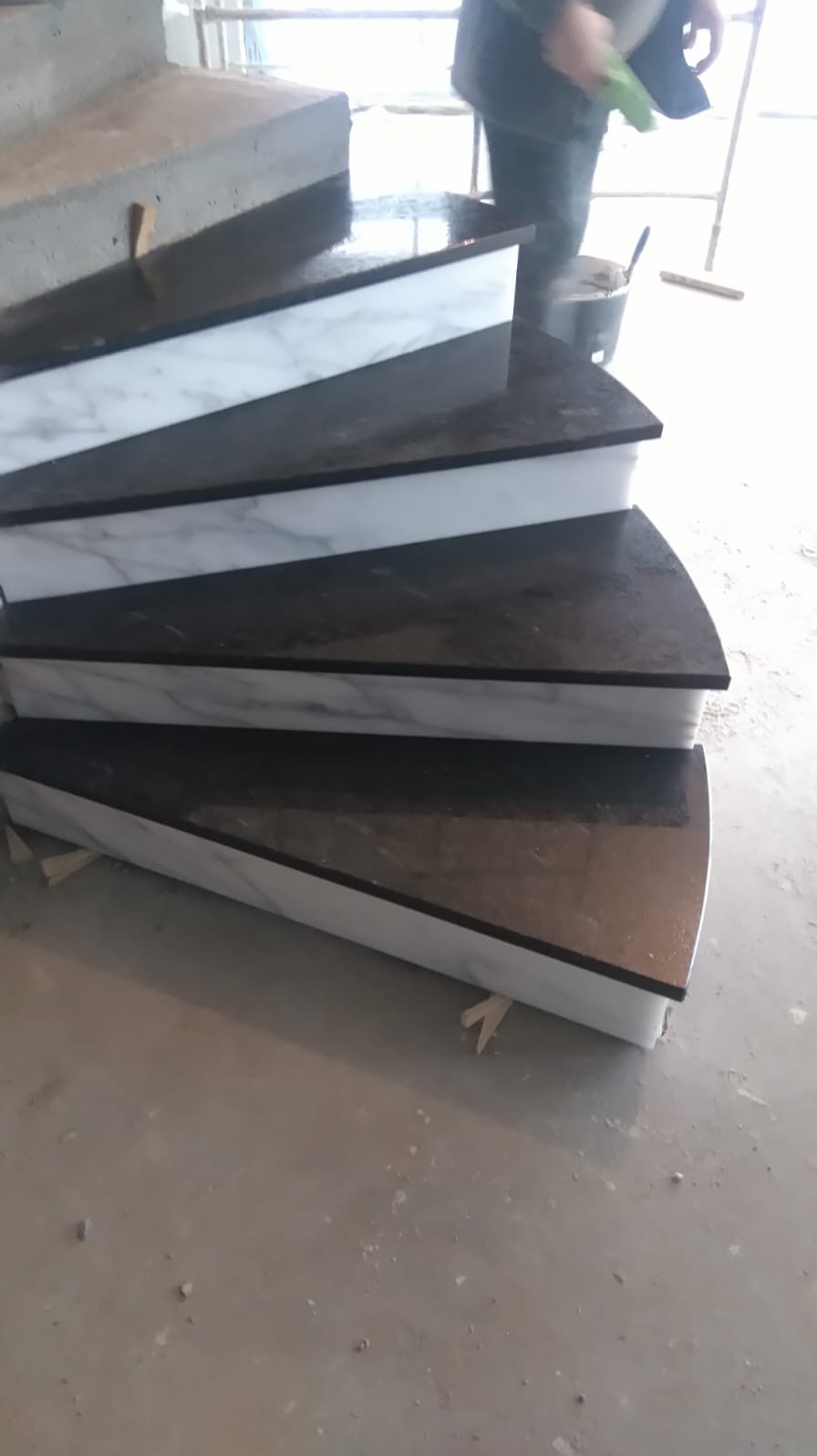 Montaż schodów z czarnego kamienia z białymi marmurowymi podstopnicami, widoczne etapy wykończeniowe i narzędzia.