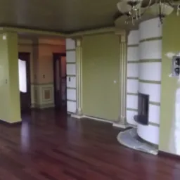 Salon z ciemną, lakierowaną podłogą, kolumnami i kominkiem w zabudowie. Ściany w odcieniach zieleni, częściowo przygotowane do malowania.