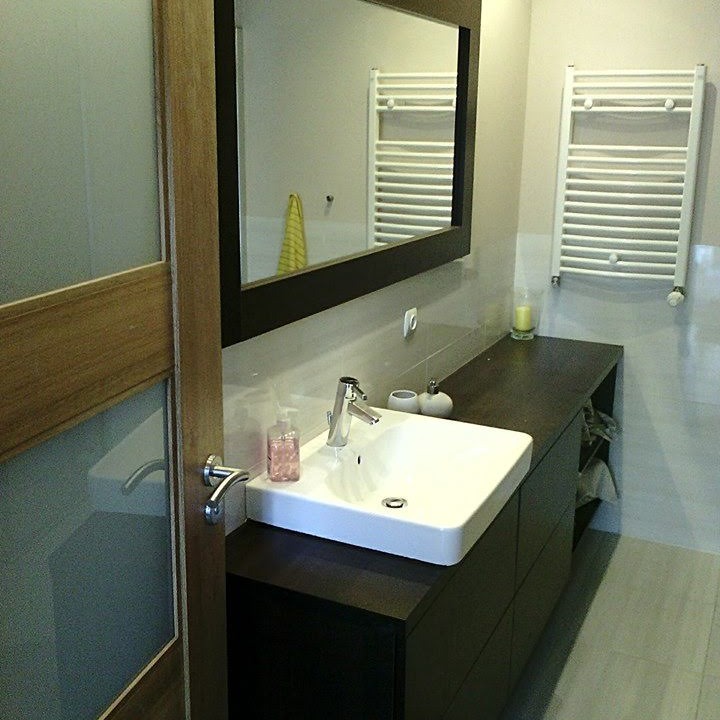 Nowoczesna łazienka z umywalką nablatową, ciemnym blatem i szafkami, lustrem w czarnej ramie oraz grzejnikiem drabinkowym.