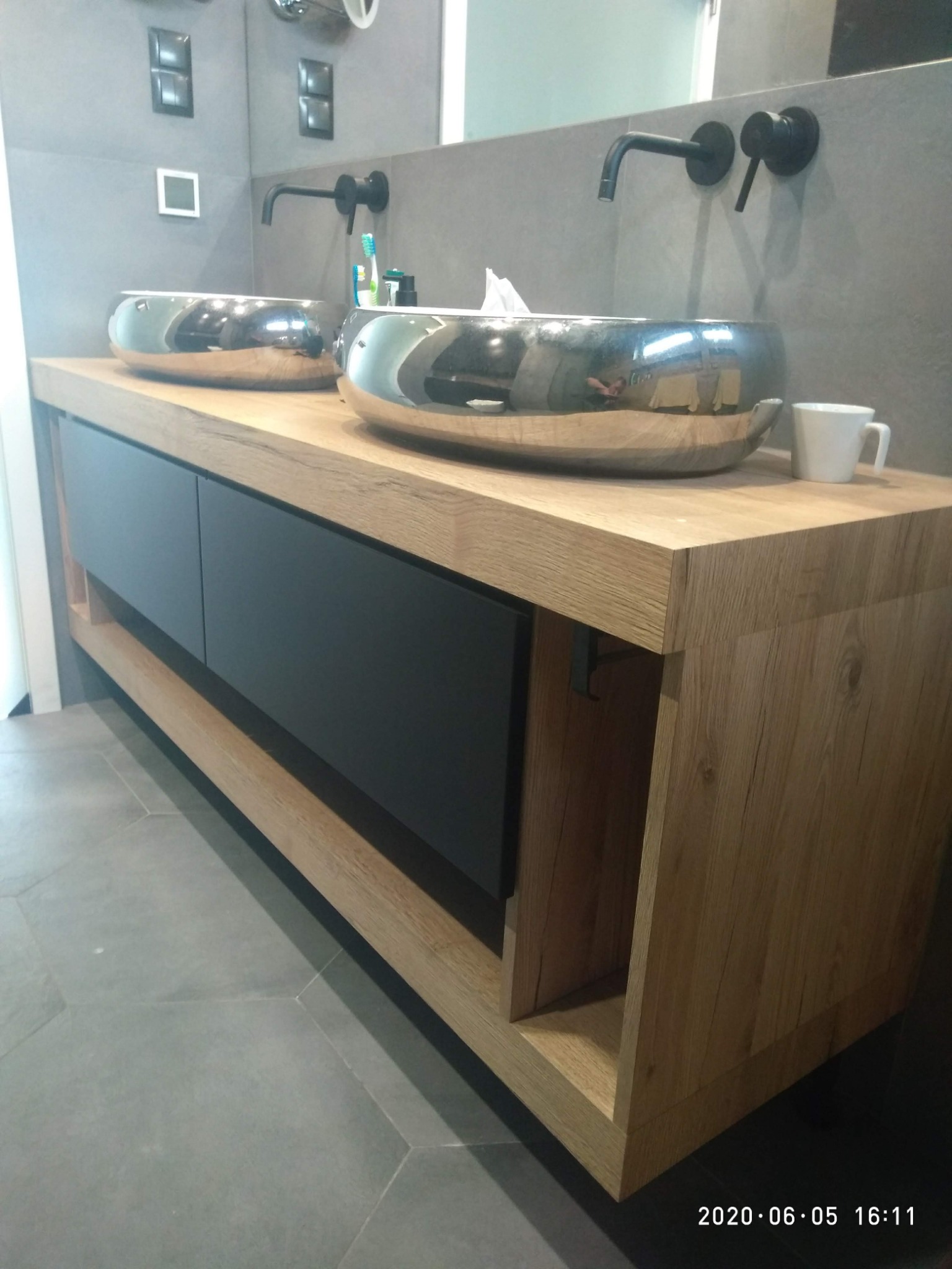 Łazienka z dwiema chromowanymi umywalkami na drewnianym blacie z czarnymi szufladami i czarną armaturą ścienną.