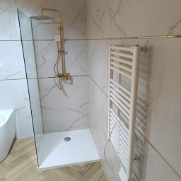 PICCOLI LAVORI - Nowoczesna łazienka z kabiną typu walk-in, złotą armaturą i grzejnikiem drabinkowym na marmurowej ścianie. Parkiet ułożony w jodełkę.